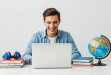 شخص يتعلم اللغة الإنجليزية بسعادة باستخدام حاسوب محمول مع كتب وسماعات رأس.